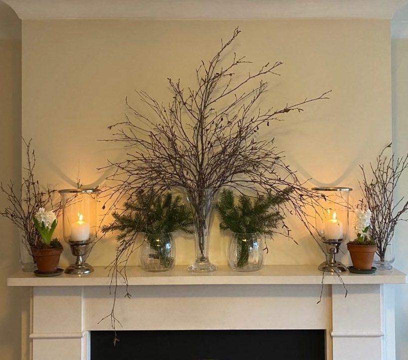 Fireplace decorated for winter with candles and greenery.